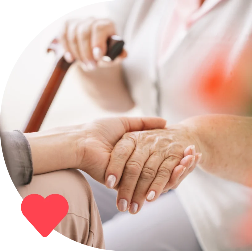 A caregiver holds an elderly person's hand, providing reassurance and support, with a heart symbol.