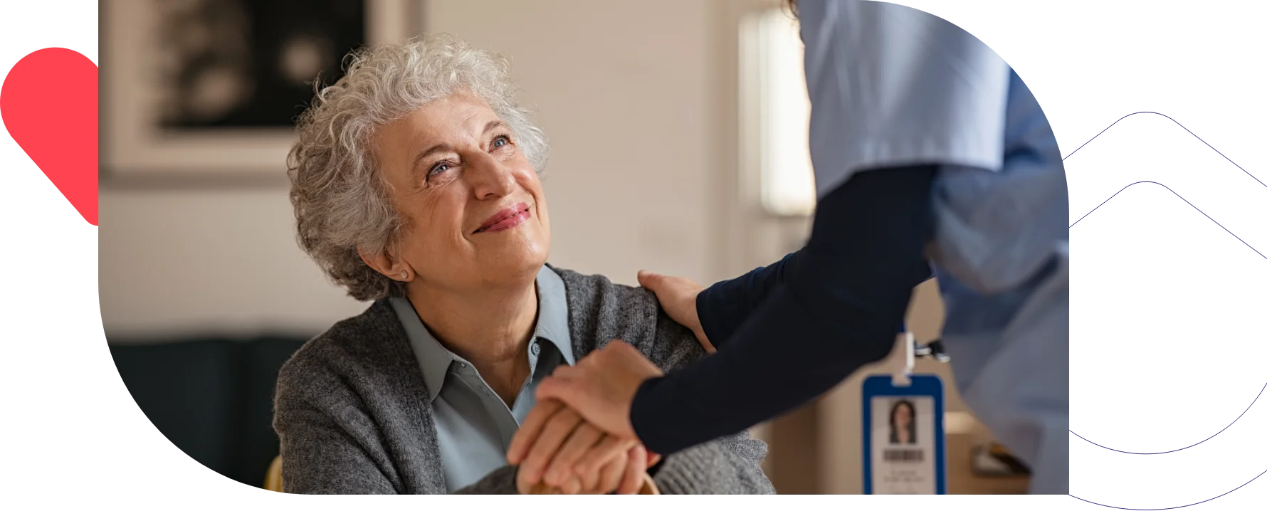 A smiling elderly woman looking up at a healthcare worker who is gently holding her hand.