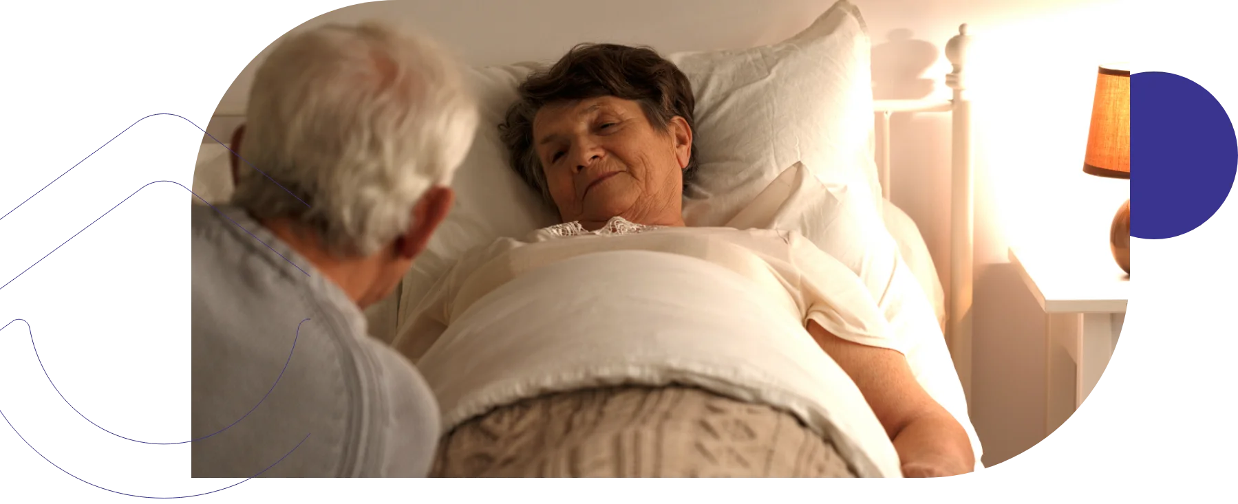 A senior woman lies in bed while an elderly man sits beside her, offering comfort or company.